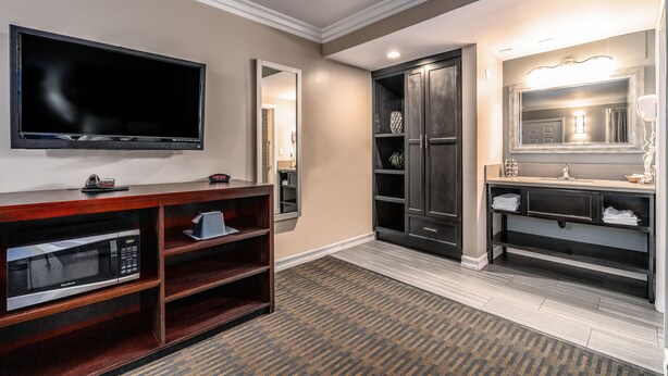 Une chambre d’hôtel équipée d’un téléviseur à écran plat, d’un four à micro-ondes, d’une coiffeuse avec miroir et d’un meuble en bois foncé.