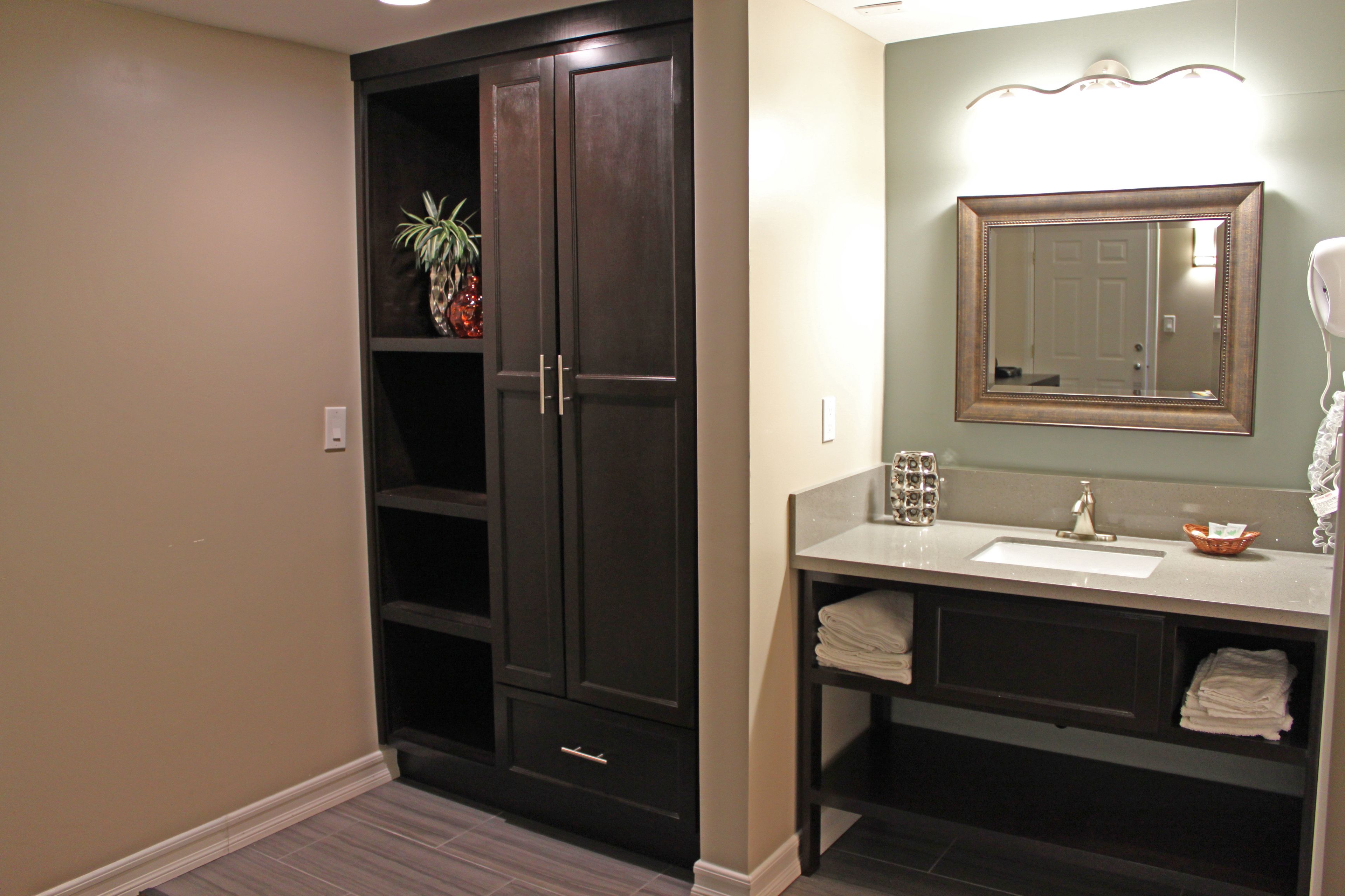 A bathroom with a dark wooden wardrobe, a sink, and a mirror.
