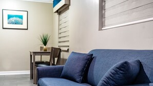 Un salon moderne avec un canapé bleu, une petite table entourée de chaises et un tableau encadré accroché au mur.