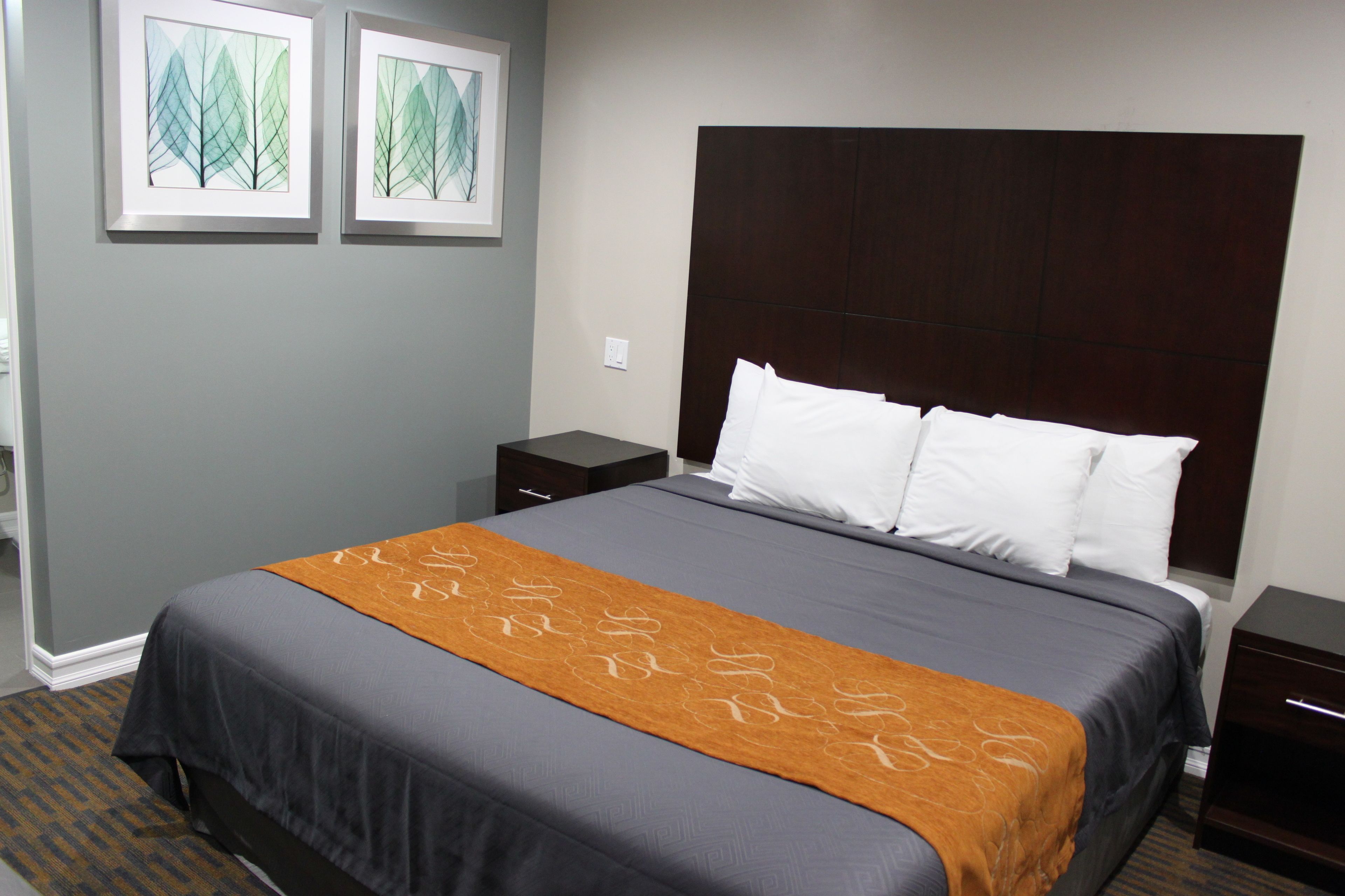 A hotel room with a large bed, a dark headboard, a brown throw blanket, and two framed artworks on the wall.