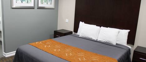 A hotel room with a large bed, a dark headboard, a brown throw blanket, and two framed artworks on the wall.