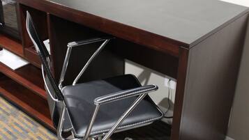 Un escritorio de madera oscura con una silla de oficina negra, un teléfono y un televisor de pantalla plana montado en la pared.