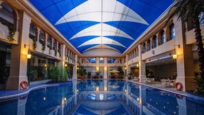 A large indoor swimming pool with a blue and white ceiling, surrounded by columns and seating areas. - Haiyun Jin Jiang Internatonal Hotel (Shenyang)