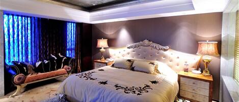 A bedroom with a large bed, two bedside tables with lamps, a decorative headboard, and a blue-lit window.