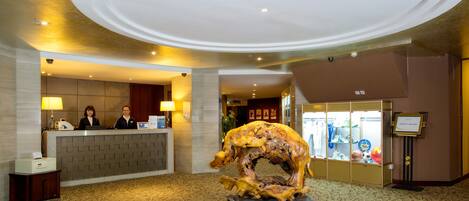 Un área de recepción con mostrador, dos recepcionistas, una gran escultura de madera y una alfombra estampada.