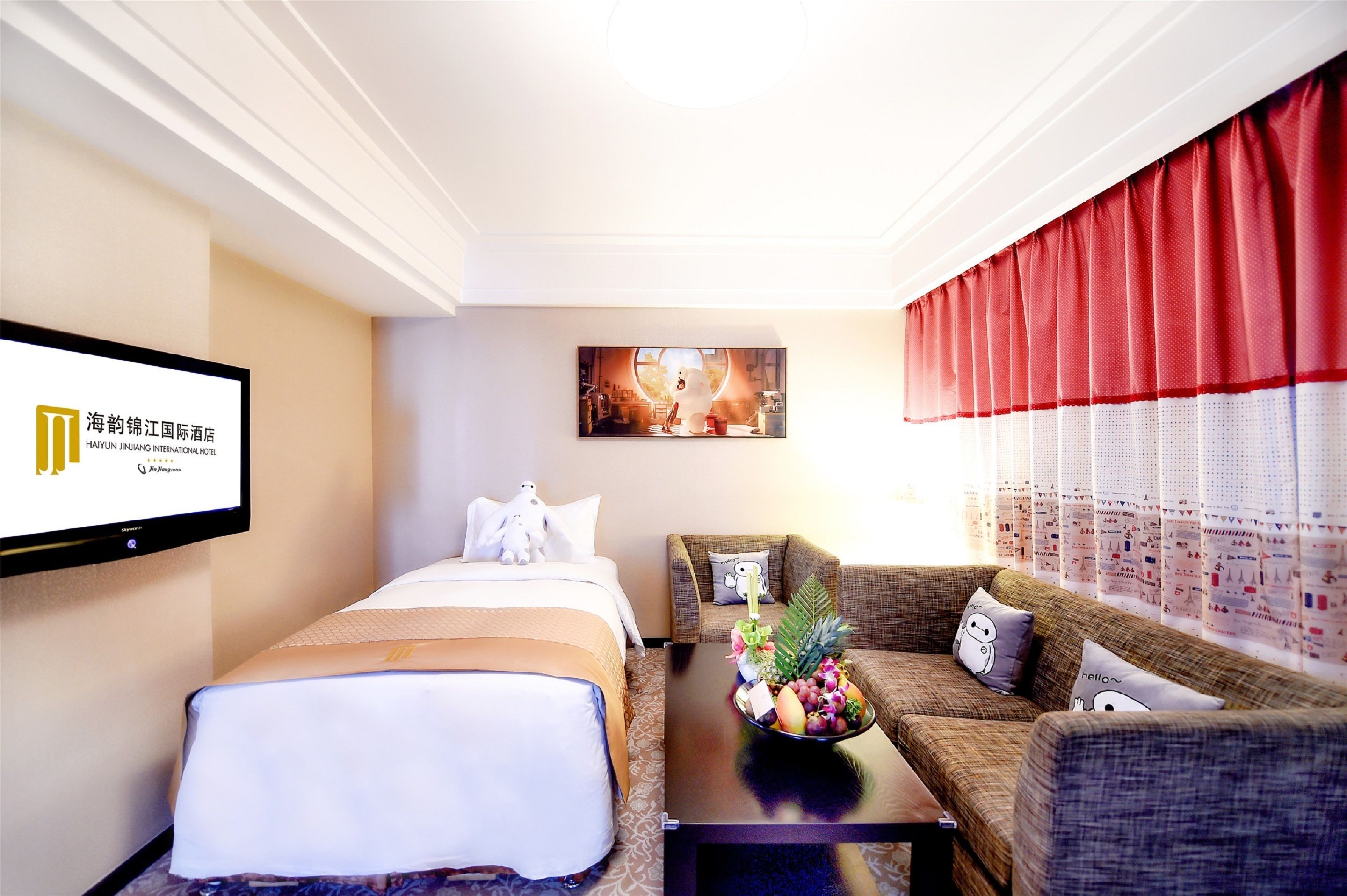 A hotel room with a bed, a sofa, a coffee table with a fruit bowl, a TV, and a painting on the wall.