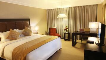 Quarto de hotel com uma cama grande, uma escrivaninha com computador, uma cadeira e uma luminária.