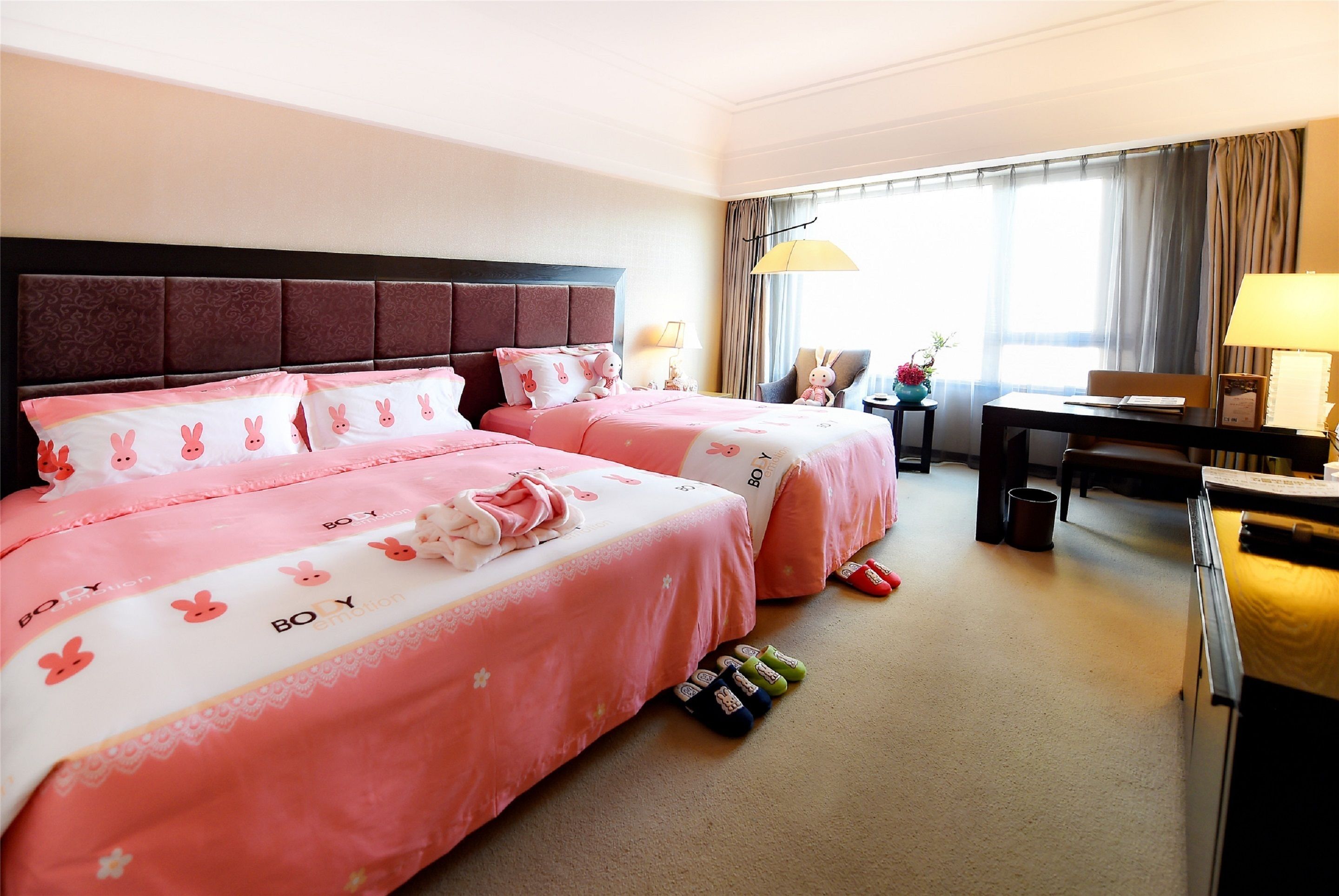 A hotel room with two beds, a desk, and a chair.