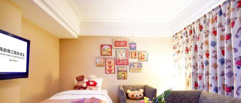Habitación de hotel con cama, sofá, mesa de centro con frutero y pared decorada con cuadros.