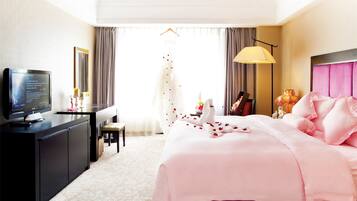 Quarto de hotel com cama, escrivaninha, televisão e janela com cortinas.