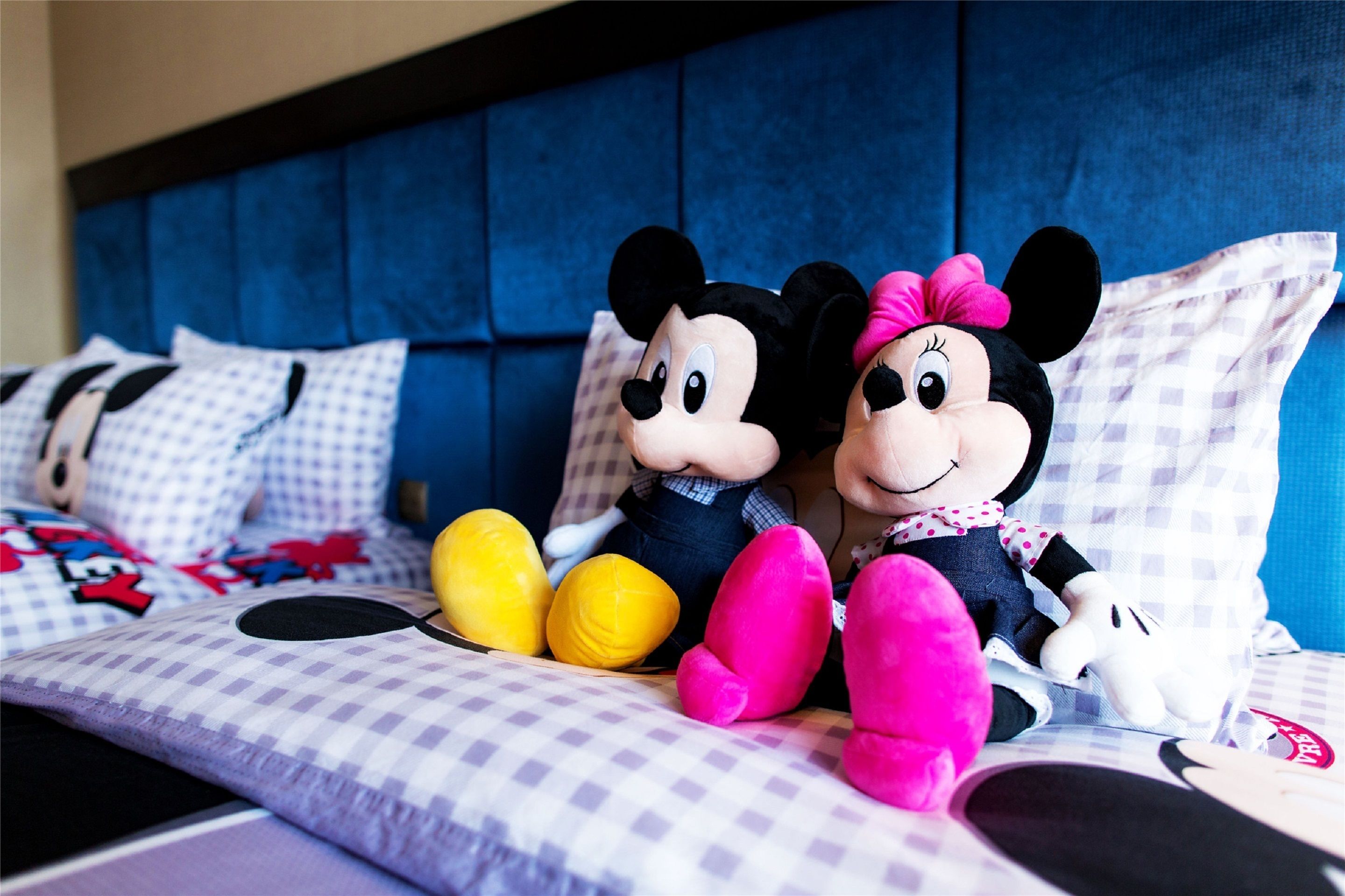 A bed with Mickey and Minnie Mouse plush toys, checkered bedding, and a blue headboard.