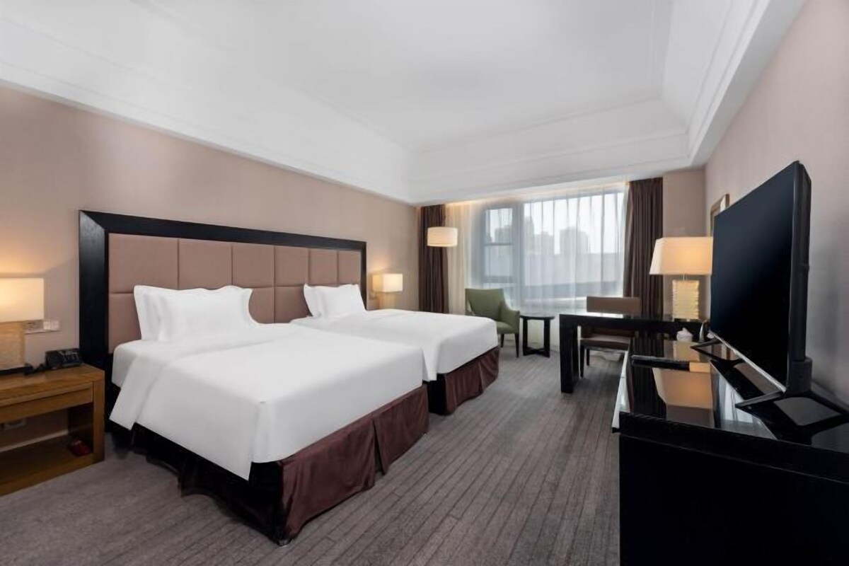 Una habitación de hotel con dos camas, un escritorio, un televisor y una ventana.