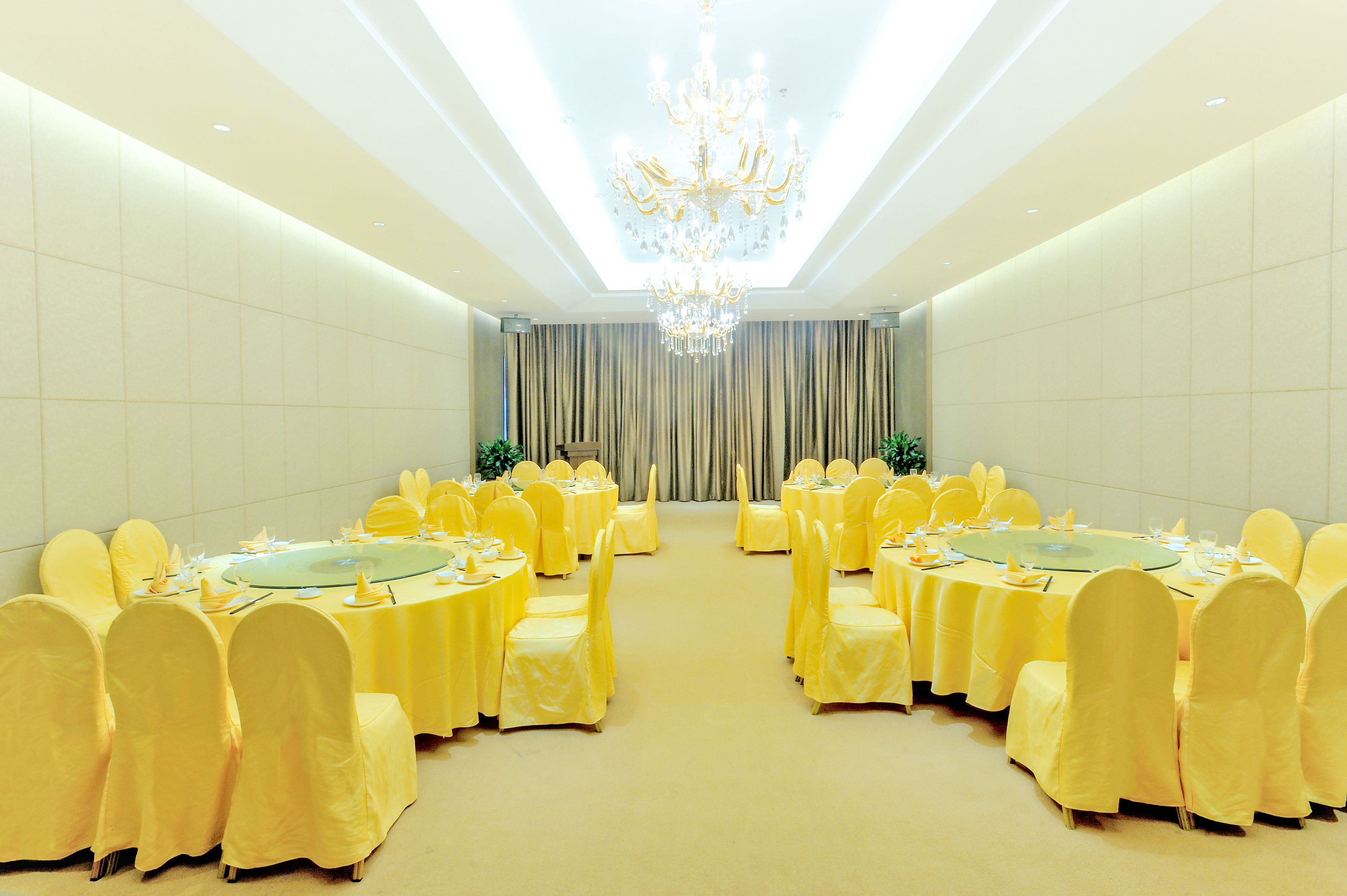 A banquet hall with round tables, yellow tablecloths, and matching chairs.