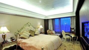 Habitación de hotel con una cama grande, un escritorio con silla, televisión y ventana con cortinas.