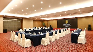 Una sala conferenze con diversi tavoli e sedie, un palco e un grande schermo che mostra il nome dell'hotel.
