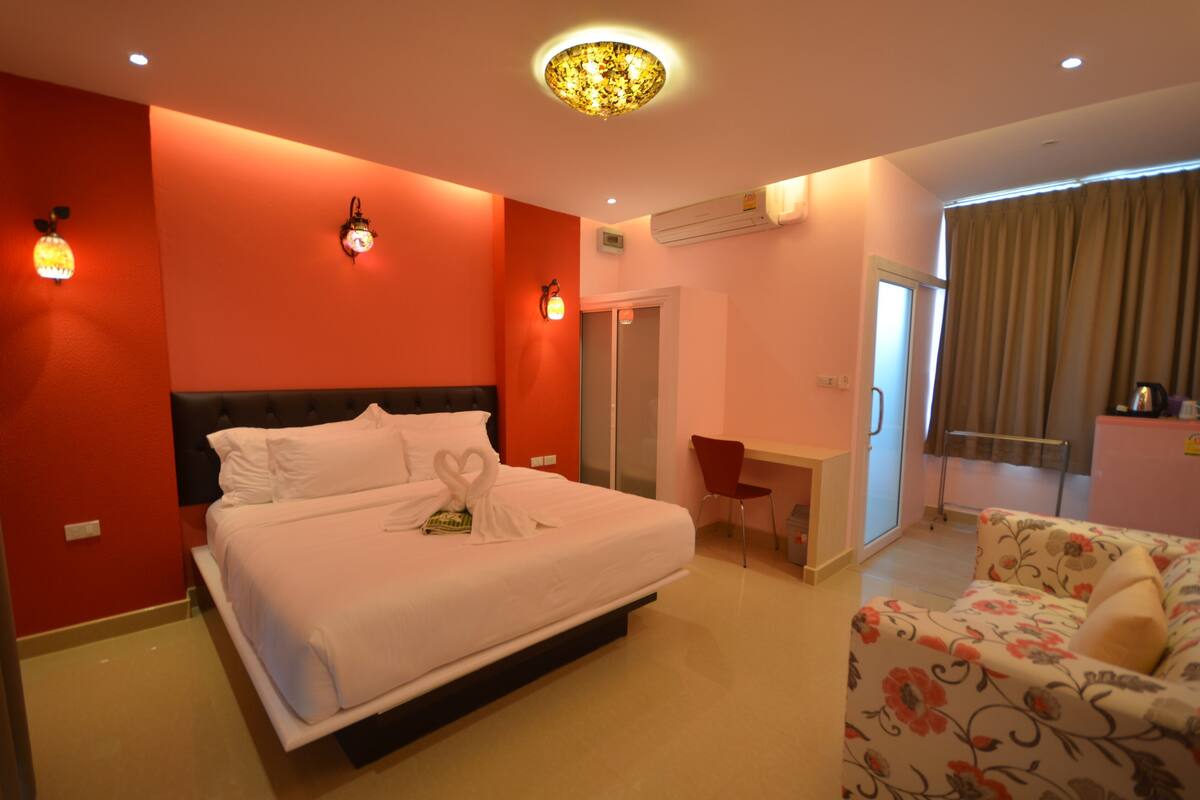 A hotel room with a large bed, a desk, a chair, and a sofa.