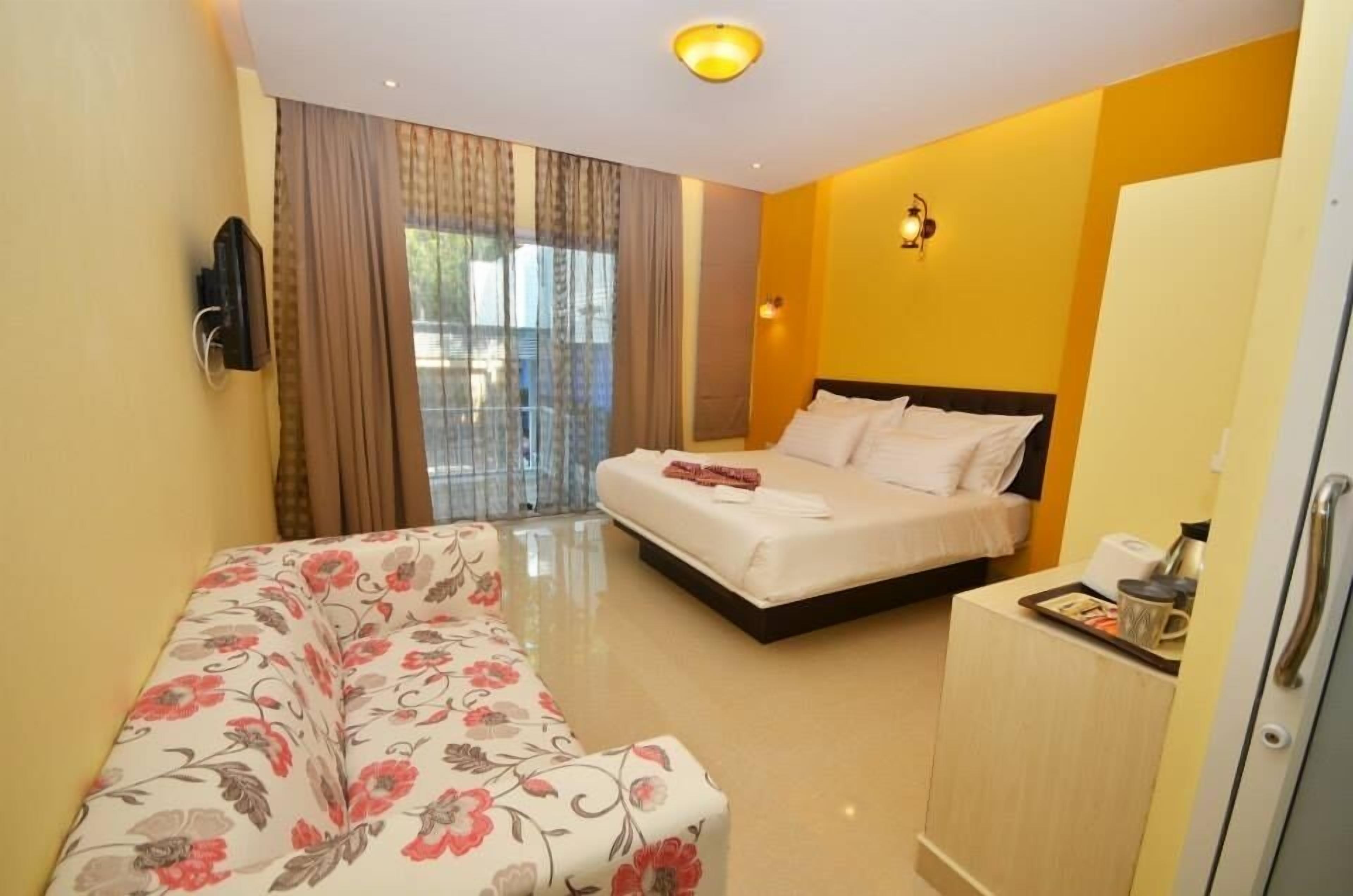A hotel room with a bed, a sofa, a TV, and a minibar.