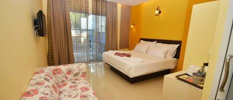 A hotel room with a bed, a sofa, a TV, and a minibar.