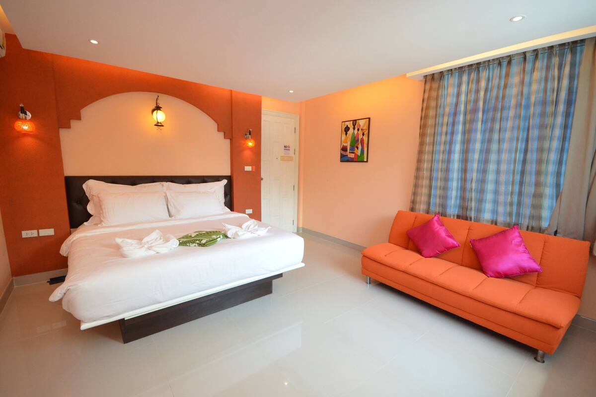 A modern hotel room with a large bed, an orange sofa, and a painting on the wall.