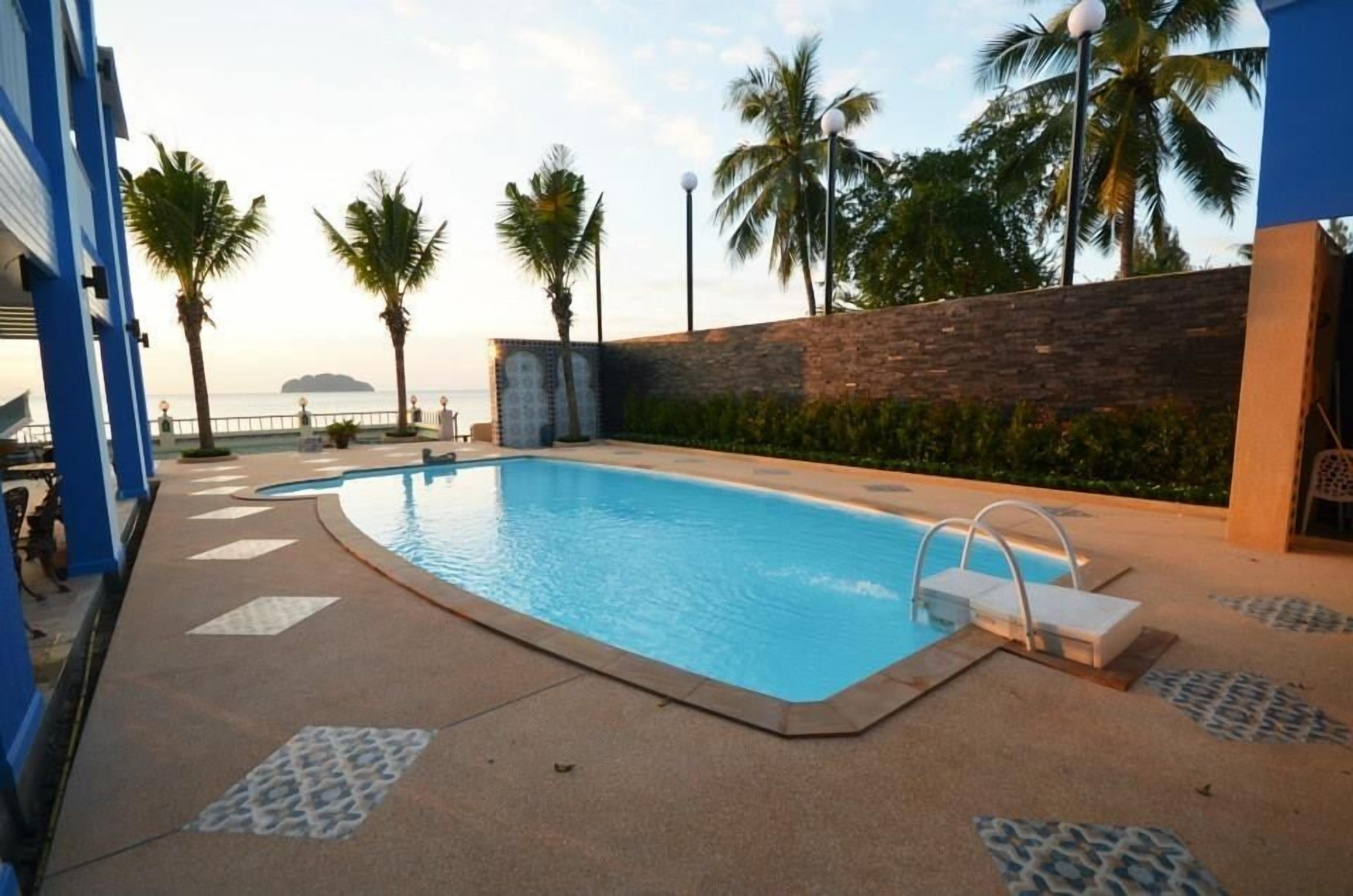A swimming pool with a tiled deck, palm trees, and a view of the sea.