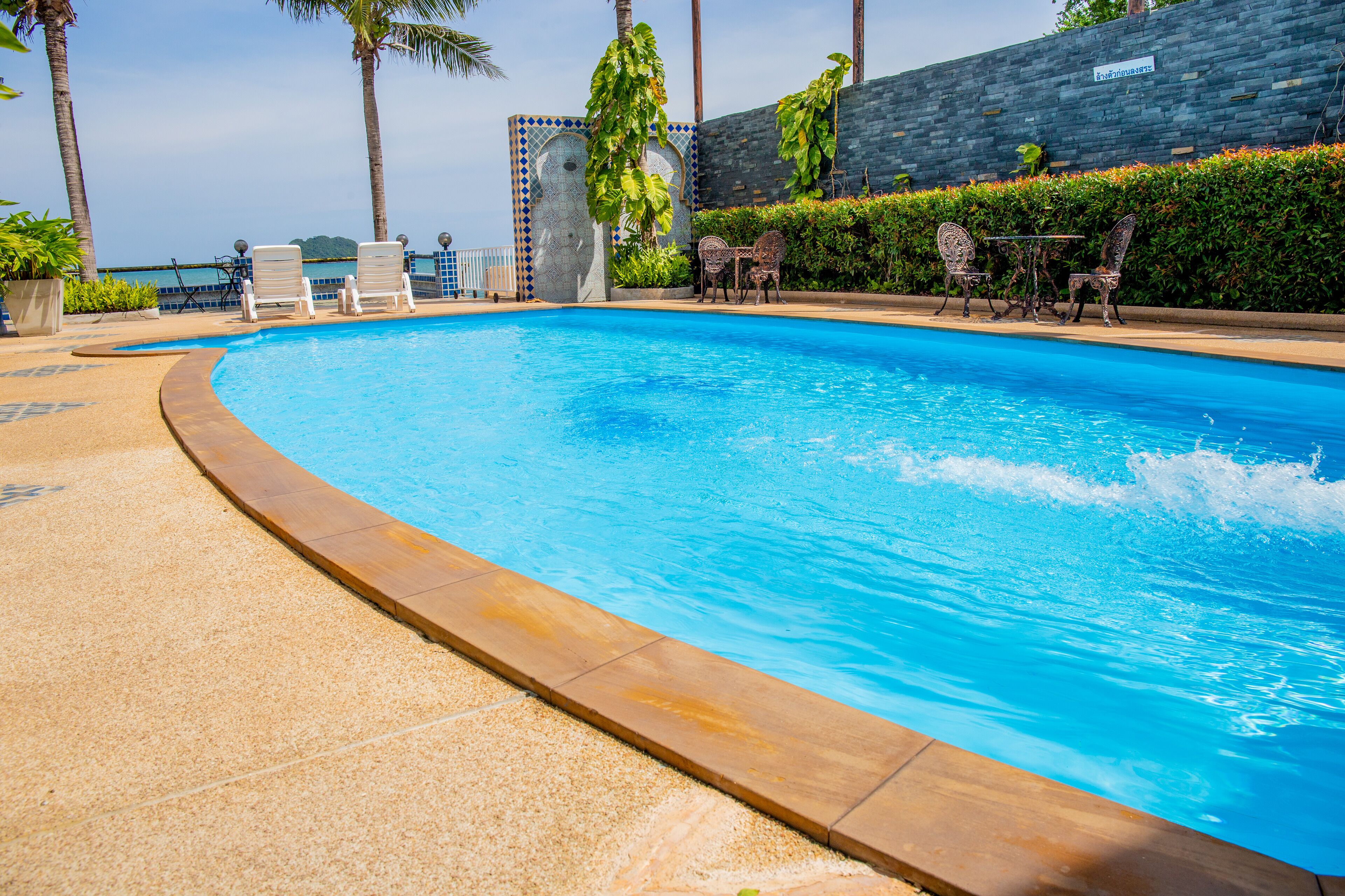 A swimming pool with lounge chairs and a table, surrounded by palm trees and a stone wall.