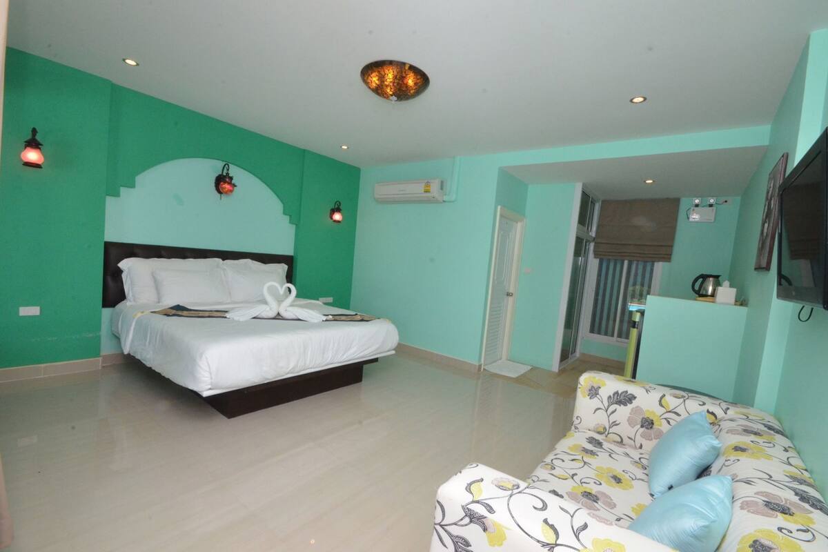 A hotel room with a bed, a sofa, a TV, and a door leading to a balcony.