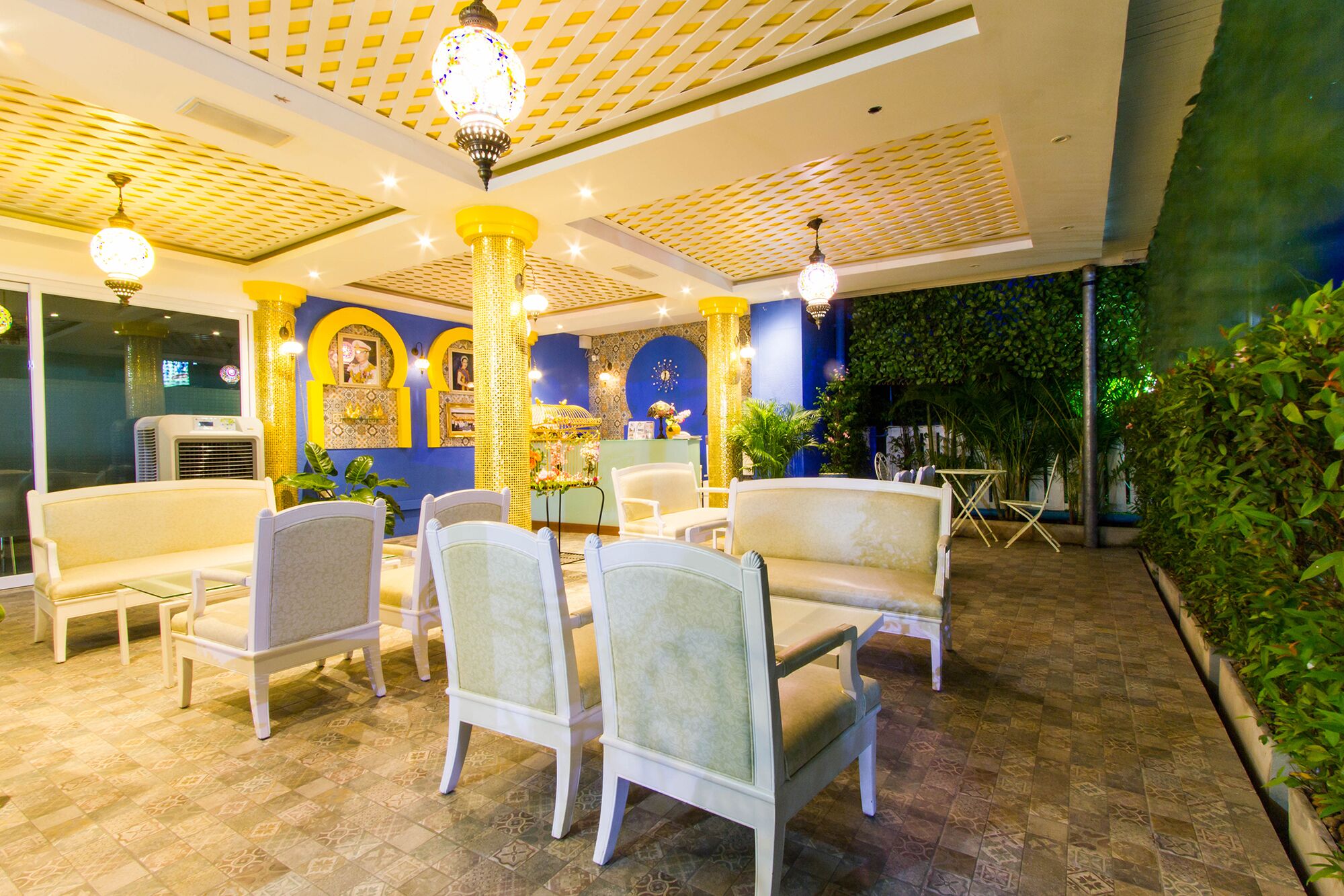 A well-lit indoor area with white chairs arranged around a table, decorative columns, and a patterned ceiling.