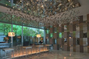 Un vestíbulo con un muro de cristal, un techo decorado con adornos colgantes y un mostrador de recepción con sillas.