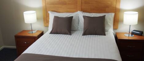 A hotel room with a large bed, two bedside tables, a wooden headboard, and a painting of a marina on the wall.