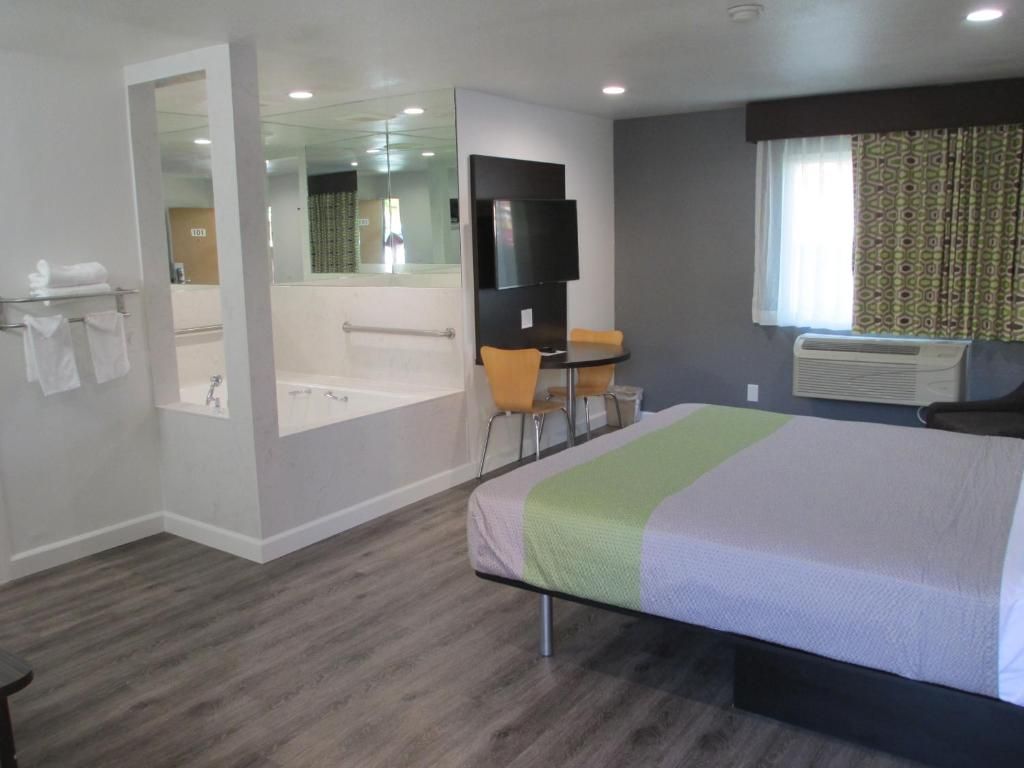 A hotel room with a bed, a seating area with a table and chairs, a bathtub, and a television.