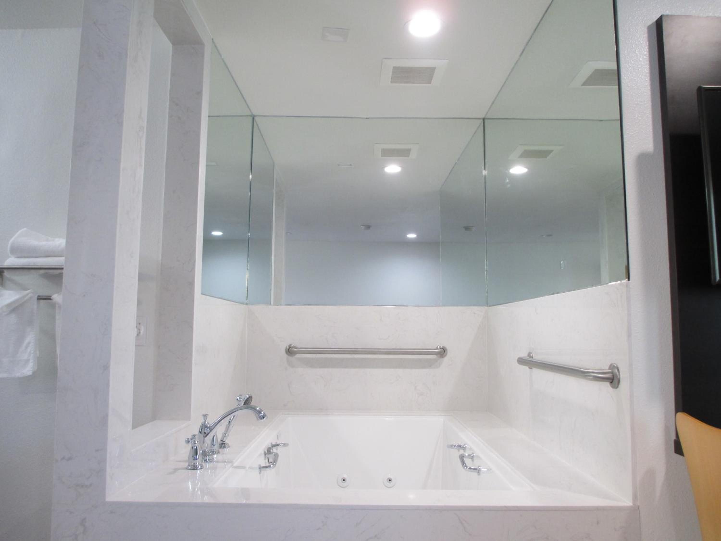 A bathroom with a large bathtub, a glass shower enclosure, and a handrail.