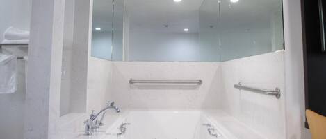 A bathroom with a large bathtub, a glass shower enclosure, and a handrail.
