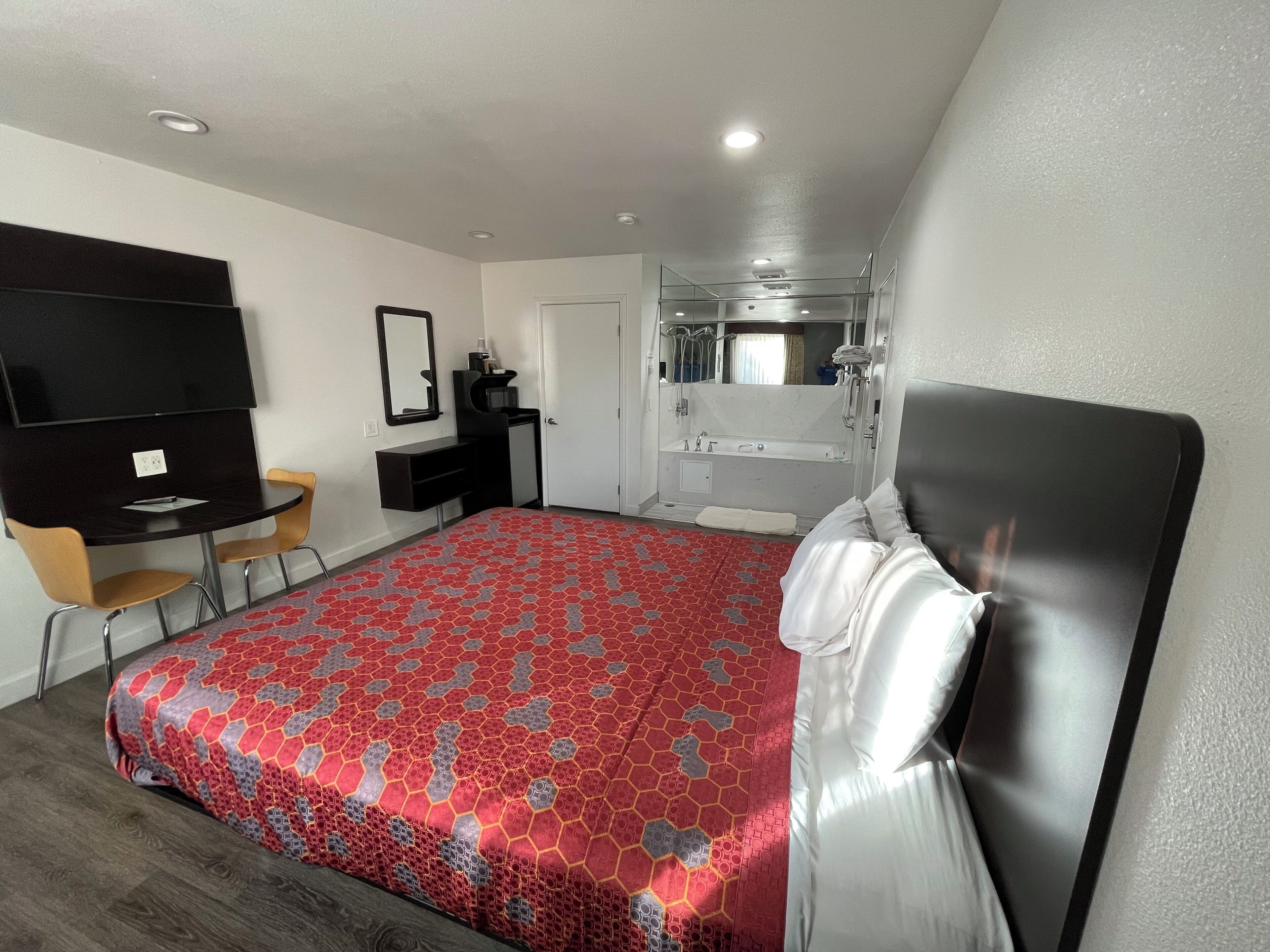 A hotel room with a large bed, a desk, a chair, a TV, and a bathroom with a bathtub and shower.