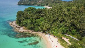 An aerial view of a tropical beach with dense palm trees, clear turquoise waters, and a sandy shore. - Ice Kamala Beach Hotel (Kamala)