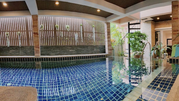 An indoor swimming pool with a tiled floor, surrounded by plants and wooden chairs. - Ice Kamala Beach Hotel (Kamala)