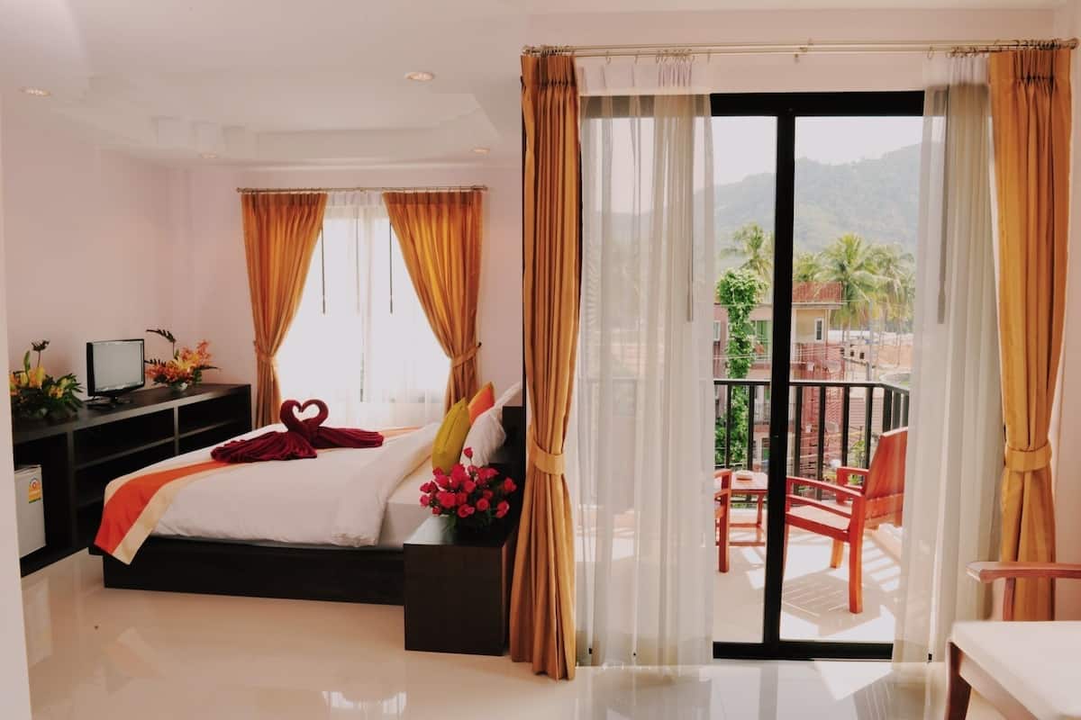 Une chambre d’hôtel avec un lit, un bureau avec un ordinateur, une télévision et un balcon avec des chaises.
