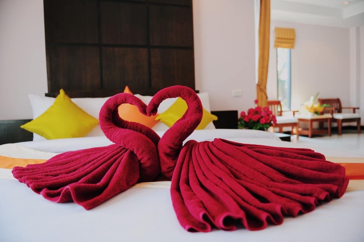 Un lit avec des serviettes rouges disposées en forme de cygnes, des oreillers jaunes et une tête de lit en bois.