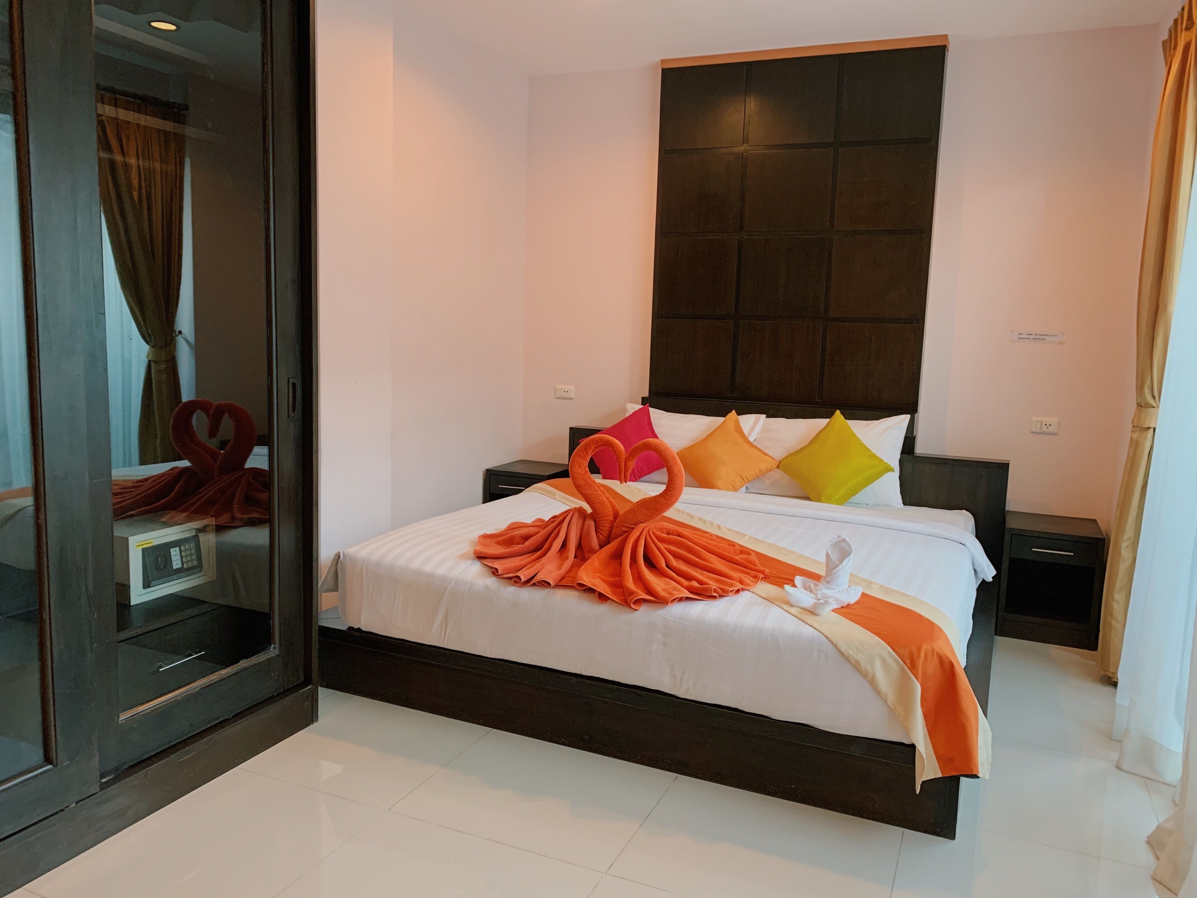 Una habitación de hotel con una cama grande, un cabecero oscuro y una puerta de cristal que da al baño.
