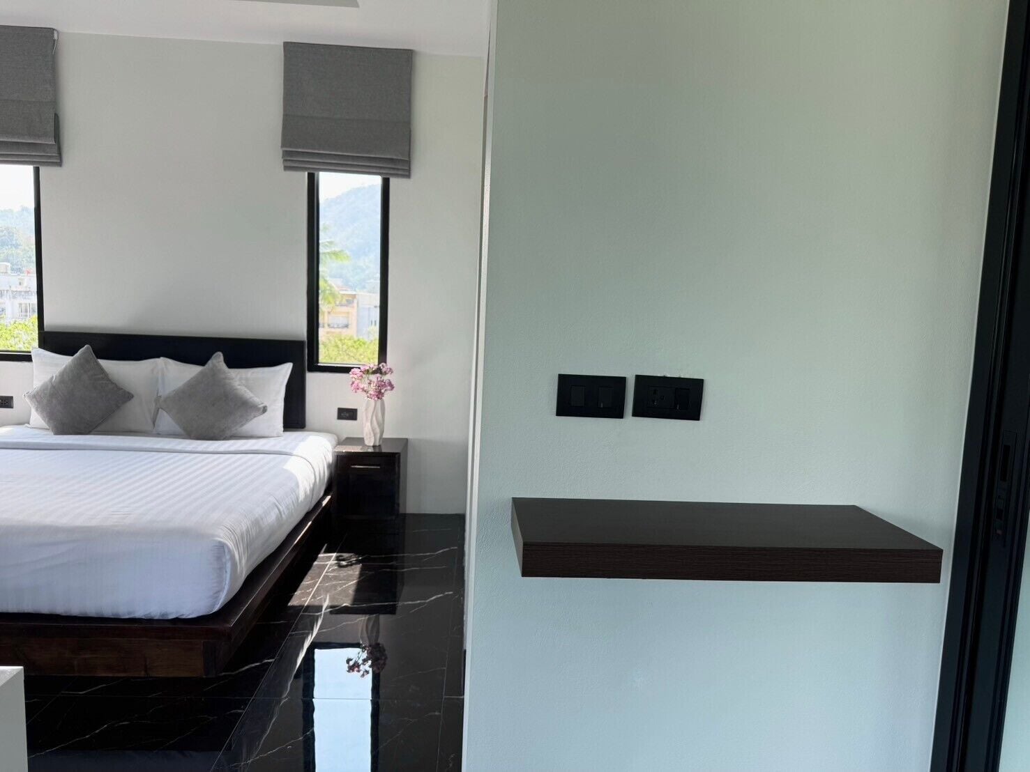 A modern bedroom with a bed, a nightstand, a vase with flowers, and a wall-mounted shelf.