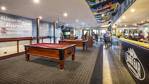 A billiards room with two pool tables, a bar area, and a mural on the wall.