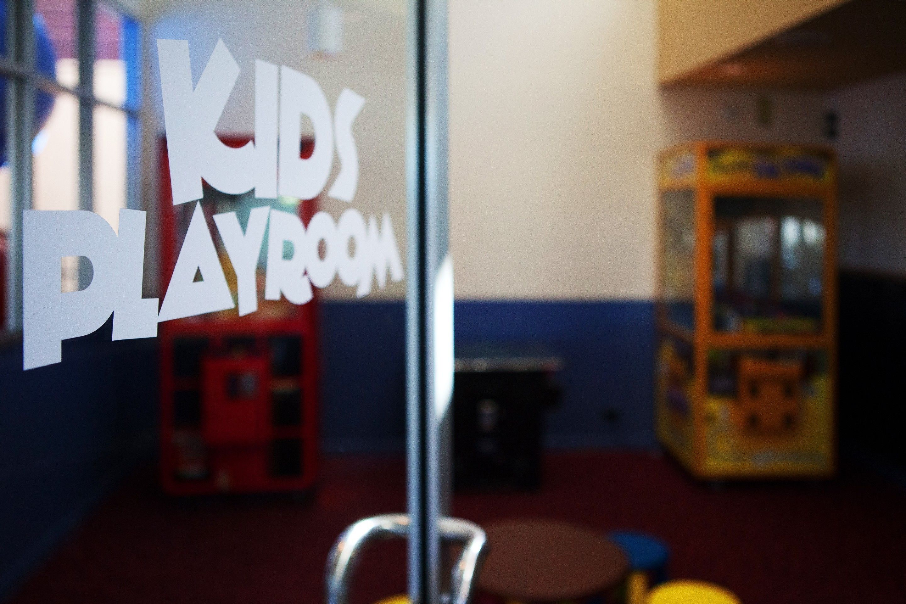 A children's playroom with a glass partition displaying the words "KIDS PLAYROOM".