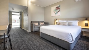 A hotel room with a large bed, a sofa, a desk, and a chair. There is a door leading to a hallway.