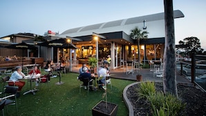 An outdoor seating area with tables and chairs, a covered patio, and a building with a modern design.