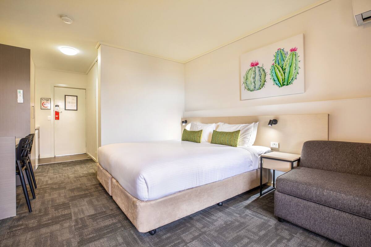 A hotel room with a large bed, a small bedside table, a chair, and a couch.