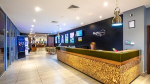 A hotel reception area with a modern design, featuring a reception desk, digital screens, and a clean, tiled floor.