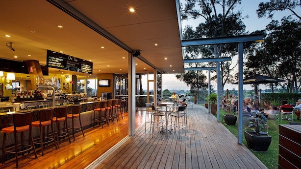 A modern bar area with a wooden floor, bar stools, and a menu board.