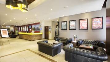 A hotel lobby with leather sofas, a reception desk, framed posters on the wall, and a modern chandelier.
