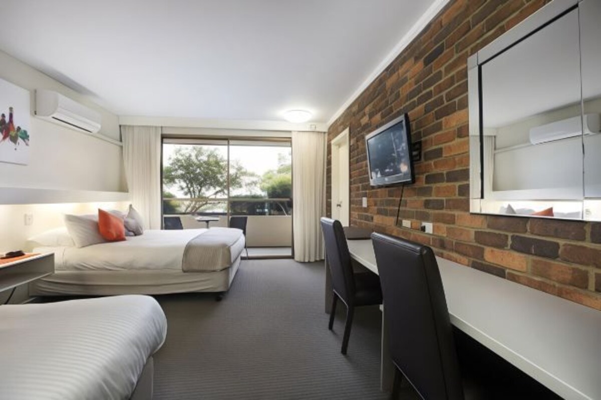 Ein Hotelzimmer mit zwei Betten, einem Schreibtisch, einem Stuhl, einem Fernseher und einem großen Fenster.