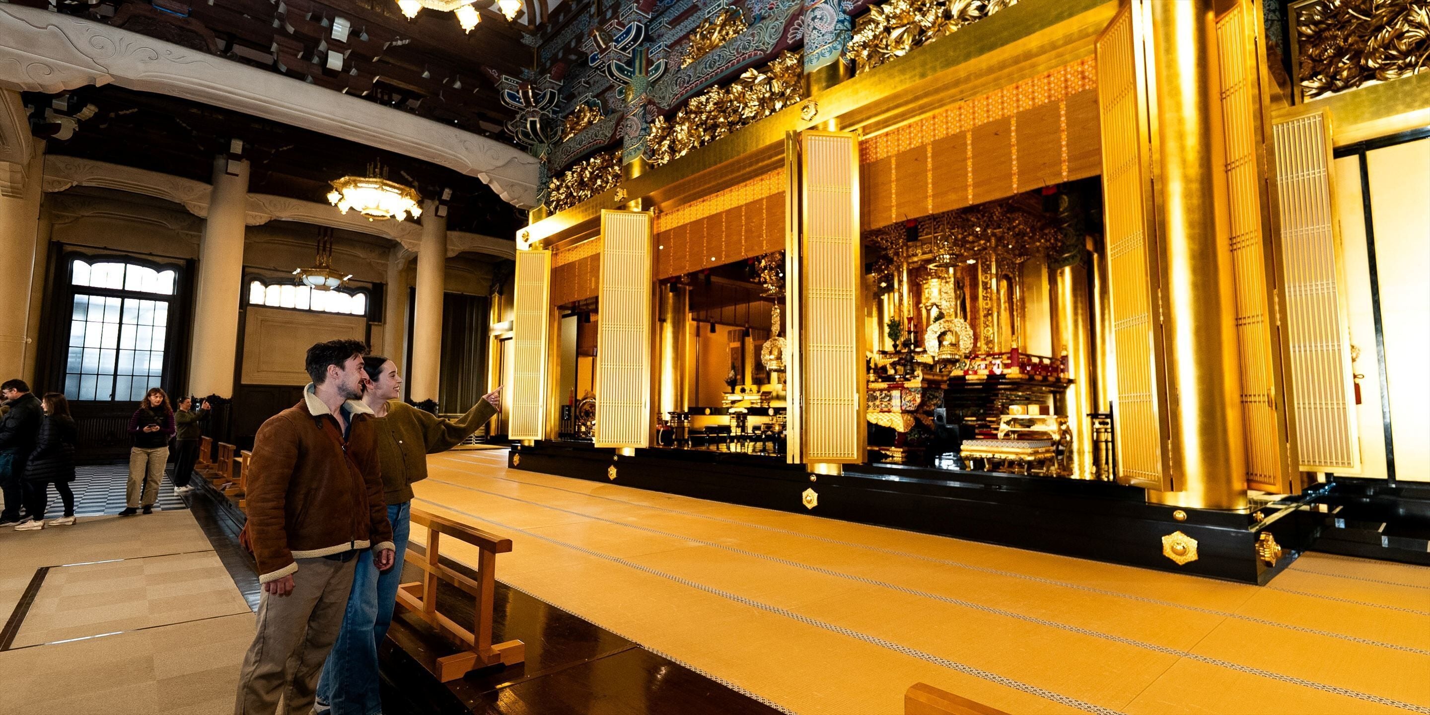 An interior with ornate golden decorations, a high ceiling, and a central aisle leading to a stage.