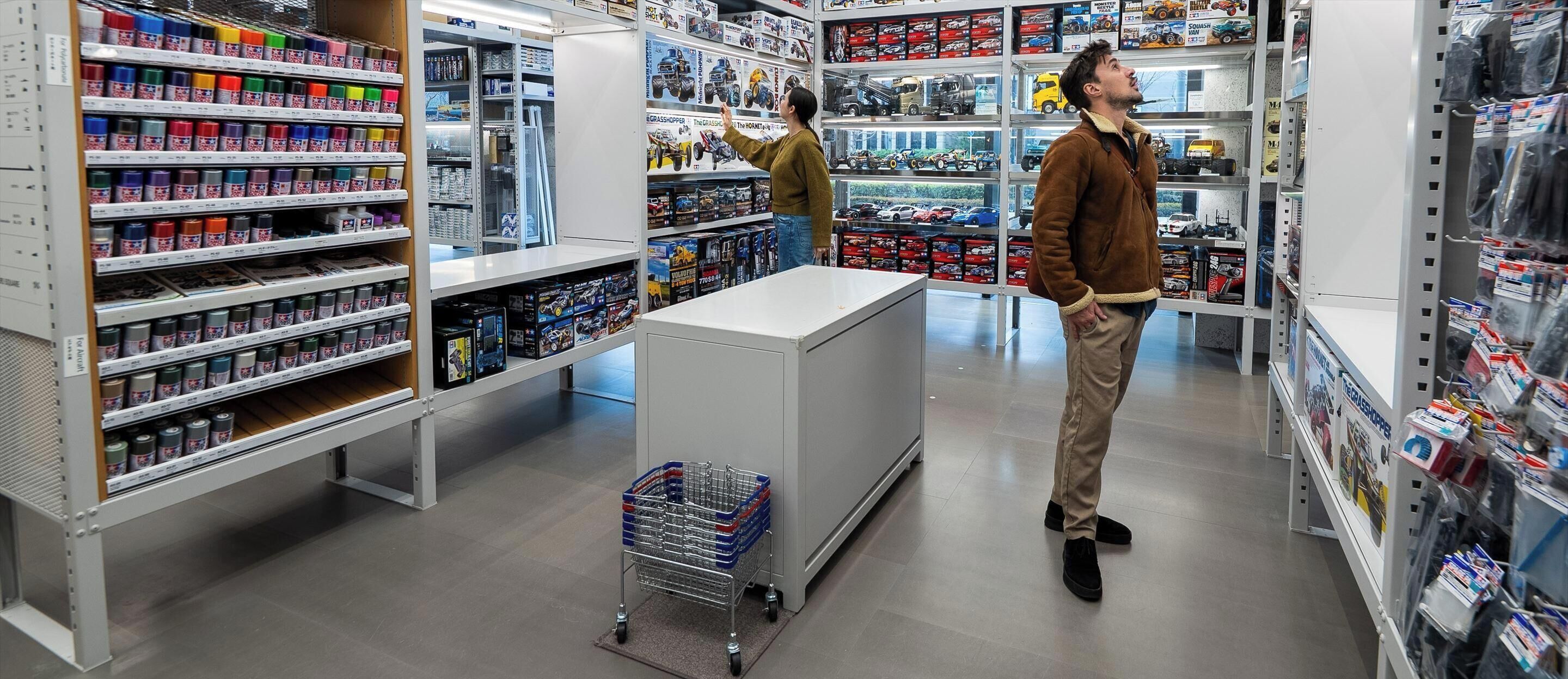 Una juguetería con estantes llenos de juguetes y juegos, un carrito de compras y una persona mirando.